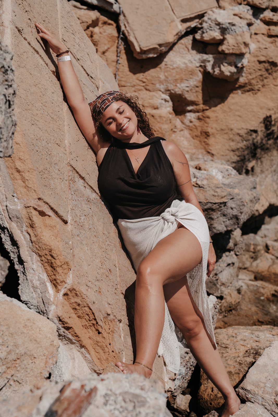 Franziska laughing, leaning against a sunny rock with her arm raised